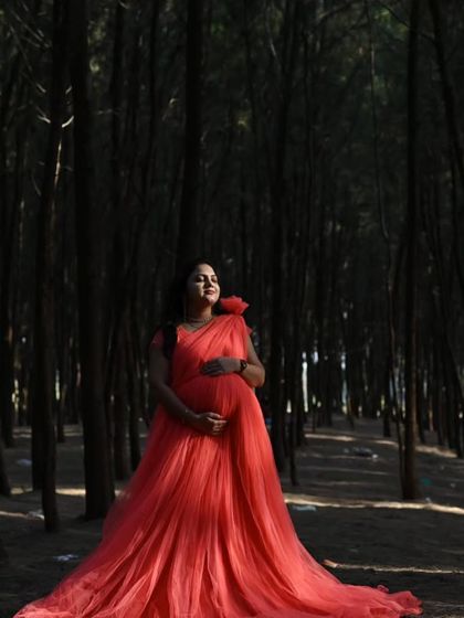 The contrast of this bright coral net gown against the dark woods creates a striking, fairytale-like image. The long trail adds to the enchanting effect.