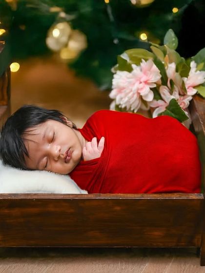 A festive Christmas scene with a newborn sleeping in a tiny bed in front of a decorated tree.