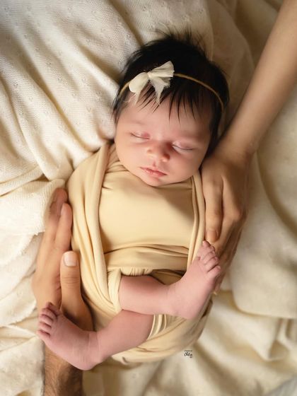 Safely swaddled and sleeping soundly. The simple cream wrap and matching headband keep this portrait feeling natural and pure, with all the focus on the baby's serene face.