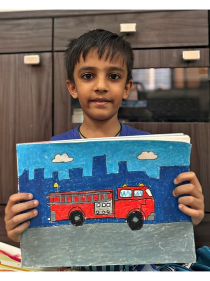 A 2nd-grade student holds his impressive drawing of a fire truck against a city skyline. We learn to draw vehicles with detail and place them in a background to tell a story.