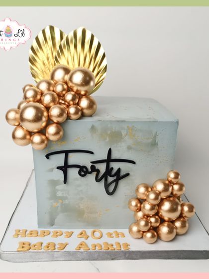 Forty and fabulous! This modern, square-tiered cake features a concrete-effect finish, accented with clusters of gold spheres and elegant gold leaf details for a glamorous 40th birthday.