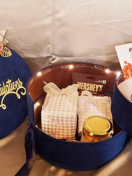 A royal blue velvet box for a special couple. This 'Congratulations' hamper opens up to reveal personalized mugs, a photo frame, and other treats, all lit up with fairy lights.