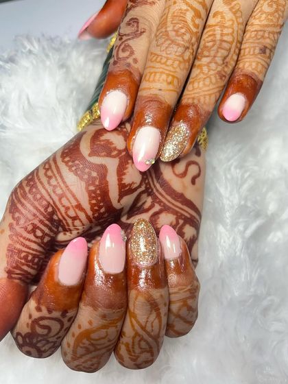 A detailed close up of the pink ombré and gold glitter bridal nails. You can see the smooth gradient transition and how the sparkle of the glitter nail catches the light, adding a touch of glamour.