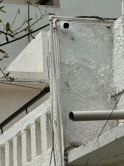 Another angle of a neatly installed outdoor camera, with the wiring protected by casing that blends in with the building's existing pipes.