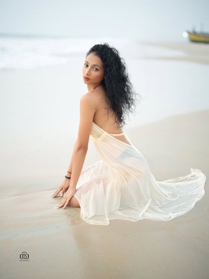 a model in a white dress on the sand. The pose is serene and the image has a soft, peaceful quality, perfect for a lifestyle or fashion lookbook.