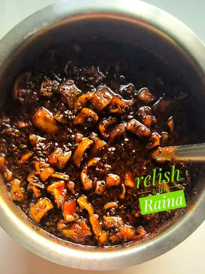Here is the sweet raw mango pickle being mixed in a large bowl. You can see the chunks of Rajapuri kairi coated in a dark, sweet, and spicy syrup made from sugar and traditional spices like fennel and onion seeds.