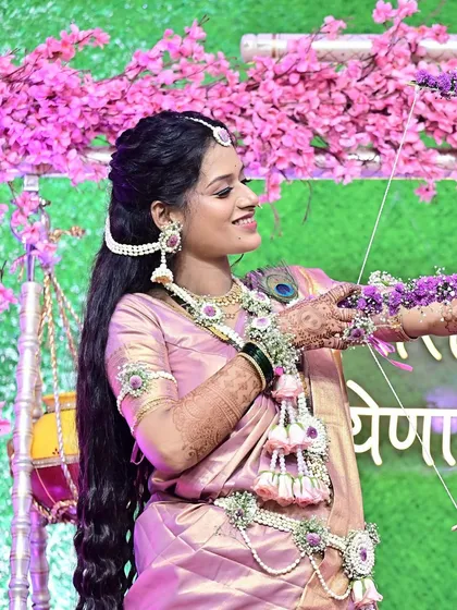 A side profile capturing the joy of the ceremony. This angle highlights the elegant hairstyle, the long, flowing hair, and the intricate details of the floral jewelry and makeup.