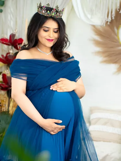 A serene moment captured in our studio. The mom-to-be wears a beautiful blue tulle gown and crown, gently cradling her baby bump amidst our botanical props.