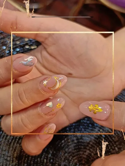 A celestial-themed set on a soft pink base. These nails are adorned with hand-placed gold and silver charms, including moons, stars, and clouds.