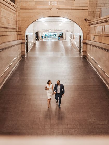 A wide shot of a couple walking hand-in-hand through an empty corridor in Grand Central Station. This image captures a quiet, private moment in an iconic public space.