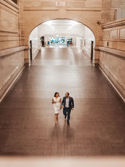 A wide shot of a couple walking hand-in-hand through an empty corridor in Grand Central Station. This image captures a quiet, private moment in an iconic public space.