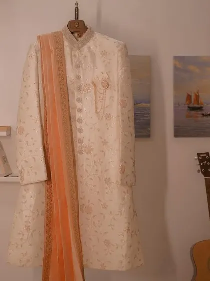 A detail shot of the groom's sherwani hanging, ready for the big day, with personal touches like a guitar and books in the room.