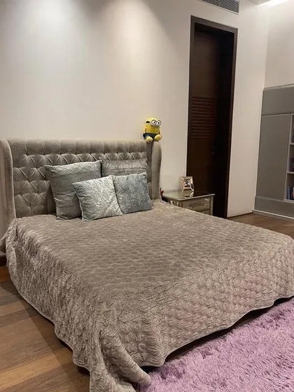 A full view of the bedroom, showcasing the elegant grey tufted wingback bed. The design balances the soft grey with the warmth of the wooden floor and the playful purple rug, creating a cohesive and stylish look.
