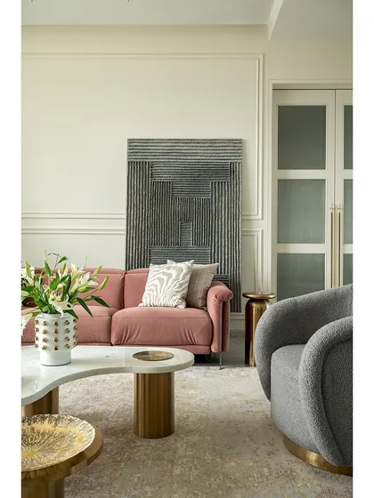 A closer look at the living room in our 2,700 sq.ft. Mumbai apartment. The combination of a plush pink sofa, a textured gray armchair, and brass accents creates a sophisticated and comfortable seating arrangement.