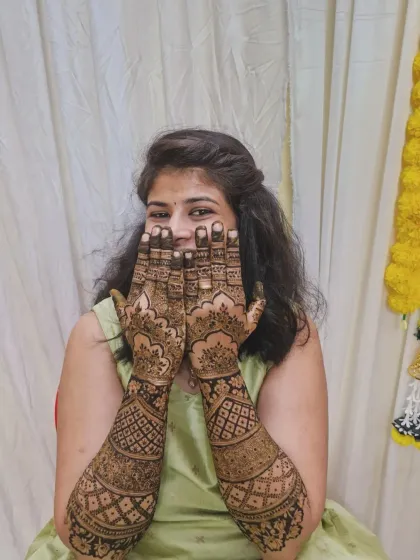 The bride shows off her full-arm traditional mehendi, which features dense, geometric patterns popular in Indian bridal art.
