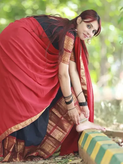 A playful and unique pose, showing the model adjusting her anklet. This adds a touch of candidness and detail to our red and black half-saree series.