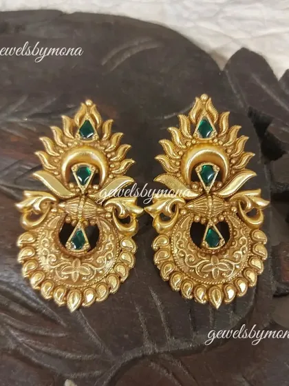A detailed shot of the beautifully crafted Dakshinaya earrings. The antique gold finish and green stone drops give them an authentic, heirloom quality.