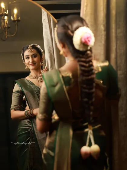 A reflective moment. This shot captures the bride's reflection in a mirror, showing both her thoughtful expression and the beautiful details of her braided hairstyle and floral adornments.