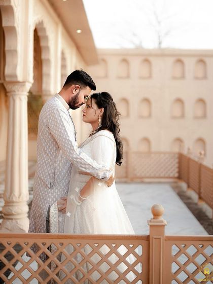 A romantic pre-wedding shot with a beautiful architectural backdrop. The bride-to-be's makeup is soft and ethereal, matching her all-white ensemble.