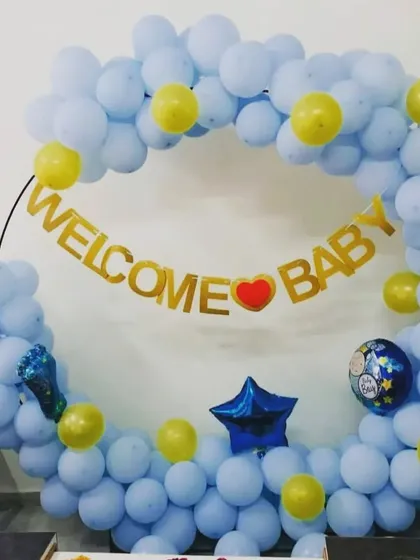A simple and sweet "Welcome Baby" decoration. The ring of light blue balloons with yellow accents and a gold foil banner is perfect for a home celebration.