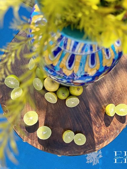 An artistic shot of sliced limes on a wooden table, with a beautifully painted ceramic vase in the background. This detail highlights the fresh, zesty elements of the Positano theme.