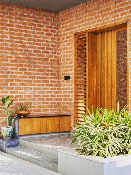 A warm and rustic entrance concept featuring an exposed brick wall. The natural texture of the brick pairs beautifully with the wooden door and simple, low-profile console table, creating an inviting and earthy entryway.