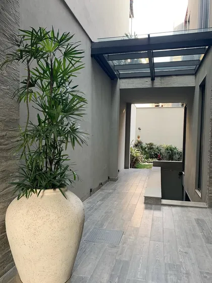 A covered walkway in a Gurgaon home, featuring a large ceramic pot and a glass skylight. The design focuses on creating beautiful transitions, with careful attention to edges, textures, and the play of light.