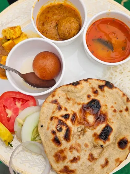 This is what a complete, satisfying meal from us looks like. Our pure vegetarian thali plate includes soft roti, rice, multiple curries, a sweet gulab jamun, and fresh salad, offering a taste of home-cooked food.