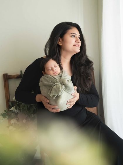 A thoughtful portrait of a new mother looking out the window, holding her baby. It’s a beautiful, contemplative image that captures the profound emotions of motherhood.