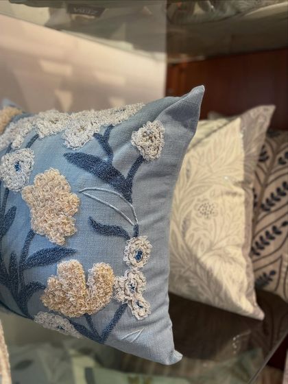 A textured floral cushion in a calming shade of blue. The flowers are created using a unique, tufted embroidery technique that gives them a three-dimensional quality, adding depth and interest to the design.