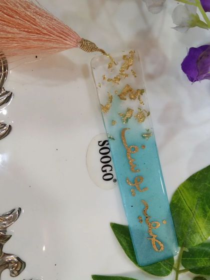 This bookmark features a name in beautiful Arabic script, set in a light blue resin with gold foil accents.