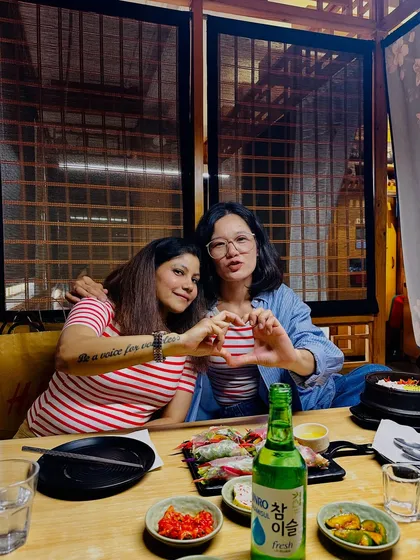 Making a heart sign with my friend over a table full of Korean food, showing my love for the culture and cuisine.