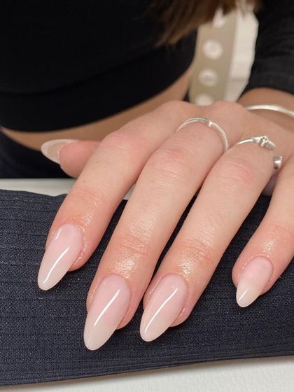 A beautiful set of long, stiletto-shaped nails with a natural, sheer pink gel polish. This look is both modern and sophisticated, showcasing healthy nails and expert shaping.