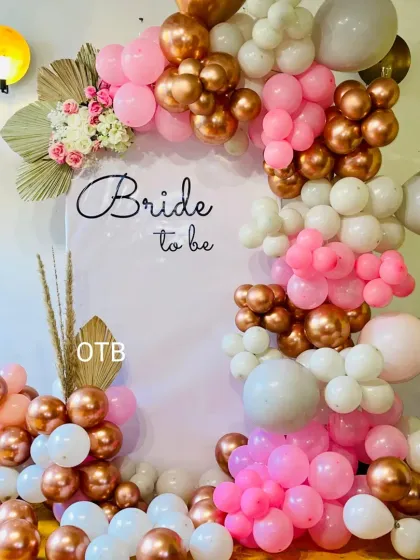 A pretty and feminine 'Bride to be' backdrop with a balloon arch in pink, white, and rose gold, accented with dried palm leaves for a boho touch.