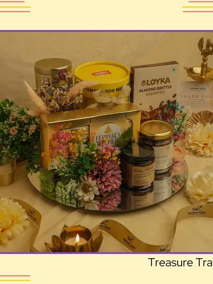 The 'Treasure Tray'. This mirrored tray is beautifully arranged with Ferrero Rocher chocolates, scented candles, and floral decorations, creating a luxurious and reflective gift.