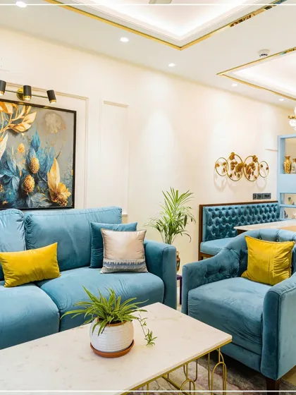 A living room with a soft blue sofa, yellow accent cushions, and gold-trimmed ceiling details, creating a fresh and calm ambiance.