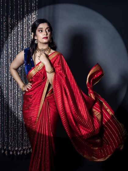 A dramatic, full-length shot. The red saree and bold lip create a powerful image, and the makeup is balanced to support this strong statement.