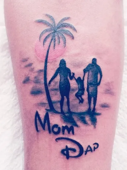 A family silhouette tattoo on the beach with "Mom Dad" written in a fun font.