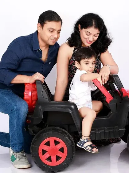 A fun and playful family portrait. The parents help their little one "drive" a toy jeep, creating a dynamic and memorable photo that captures the joy of childhood.