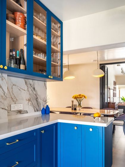 An open kitchen layout allows for seamless interaction between the kitchen and dining areas. Here, the vibrant blue cabinetry is visible from the dining table, creating a cohesive and social atmosphere perfect for hosting friends and family.