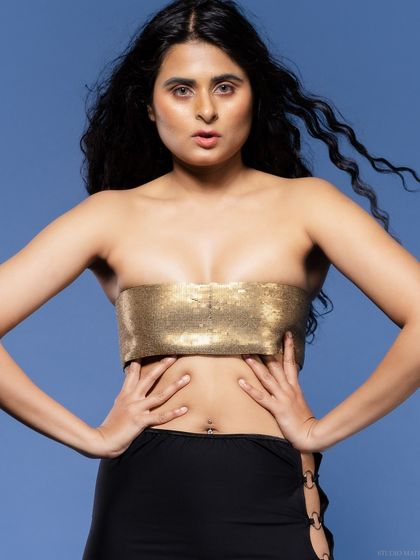 A close-up of a model in a gold bandeau top, with a confident and direct gaze.