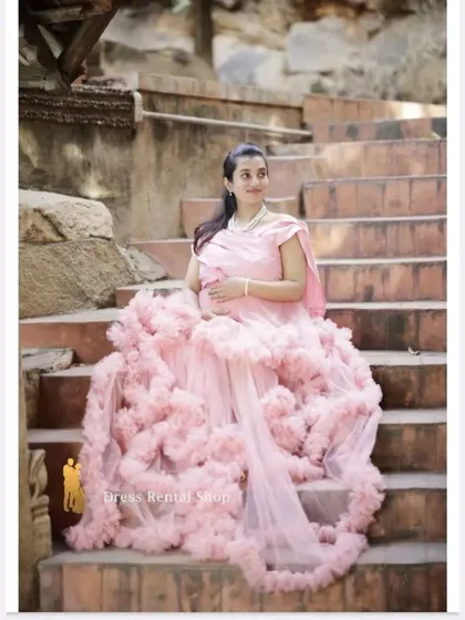 This shot on a staircase showcases the beautiful drape of the pink ruffled gown's train. It's a perfect setting to display the full volume and romantic texture of this rental dress.