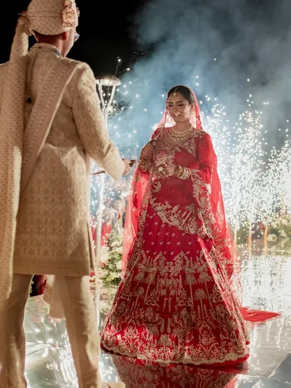 The bride and groom meet on the mirrored stage, surrounded by the glow of pyrotechnics. This shot captures the joy and excitement of the Varmaala moment, amplified by the dramatic special effects.