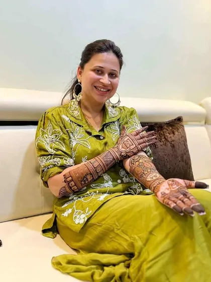 A smiling client relaxing on a sofa, happy with her full bridal mehendi.