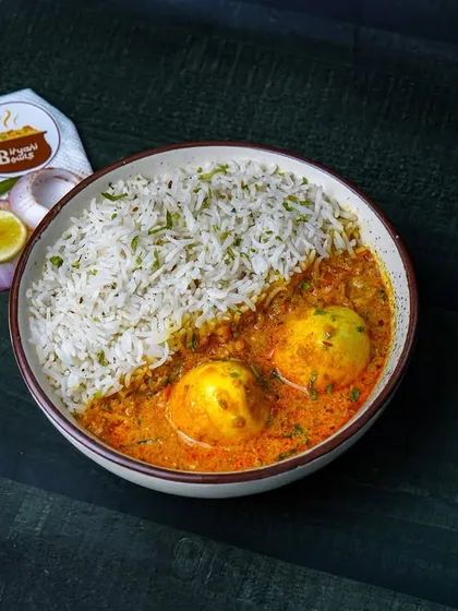 A comforting bowl of egg curry served with steamed rice, shot on a dark wooden background. The moody lighting creates a warm, homely feeling, perfect for promoting comfort food.