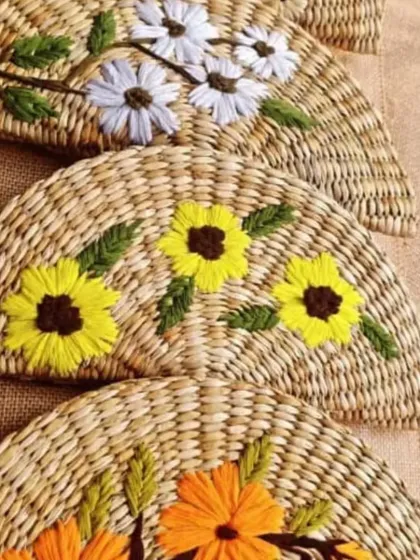 The detailed embroidery on our fan-shaped clutches is a testament to artisan skill. This image displays three different floral patterns, from white daisies to yellow sunflowers, each adding a unique personality to the handwoven base.