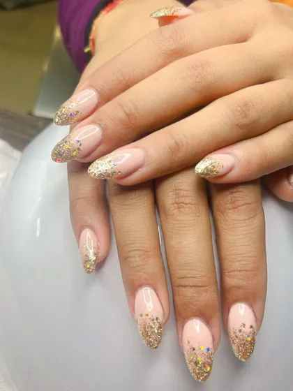 A beautiful example of a glitter fade on long almond nails. This design blends a natural pink base into a sparkling gold glitter tip, making it a popular choice for weddings and celebrations.