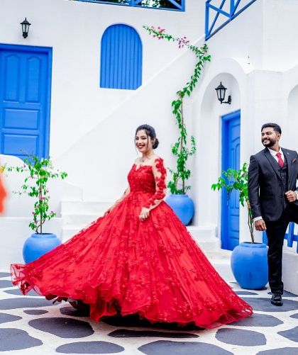 A playful, candid moment from a couple's photoshoot. The full skirt of the red ball gown adds a touch of grandeur and fun to the scene.