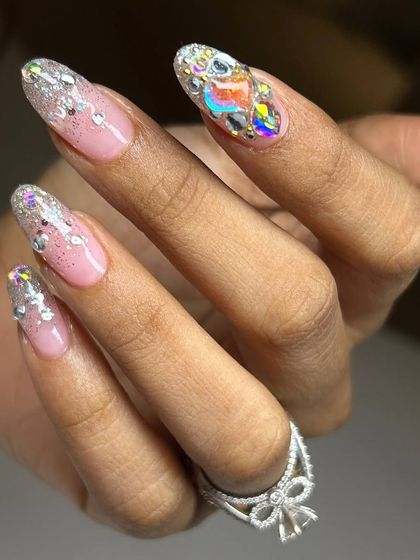A glamorous set of nail extensions featuring a glittery French tip and a fully encrusted accent nail with large, iridescent rhinestones for maximum sparkle.