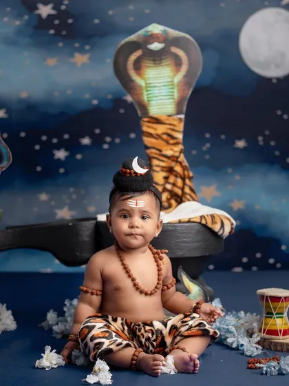 A serene portrait of a baby dressed as Lord Shiva, sitting peacefully with a cobra and trishul in the background.
